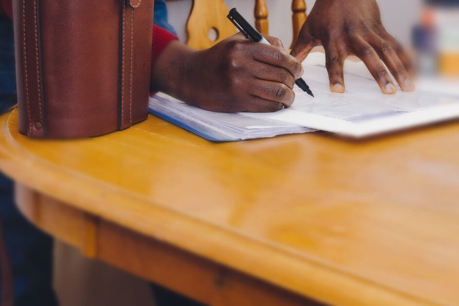 DBS changes for dance teachers: new rules and lower fees Hands filling in a paper form with a pen at a wooden table, the kind of paperwork that DBS changes can affect for dance teachers