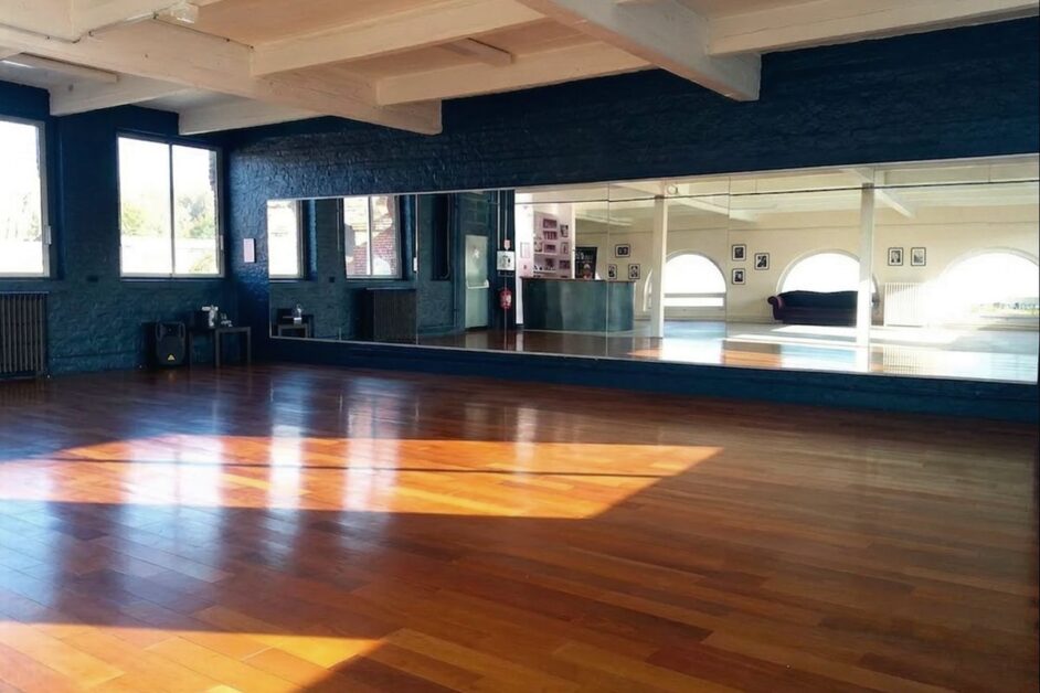 Empty, sunlit dance studio with a wooden floor and a long mirror wall, ready for a summer intensive